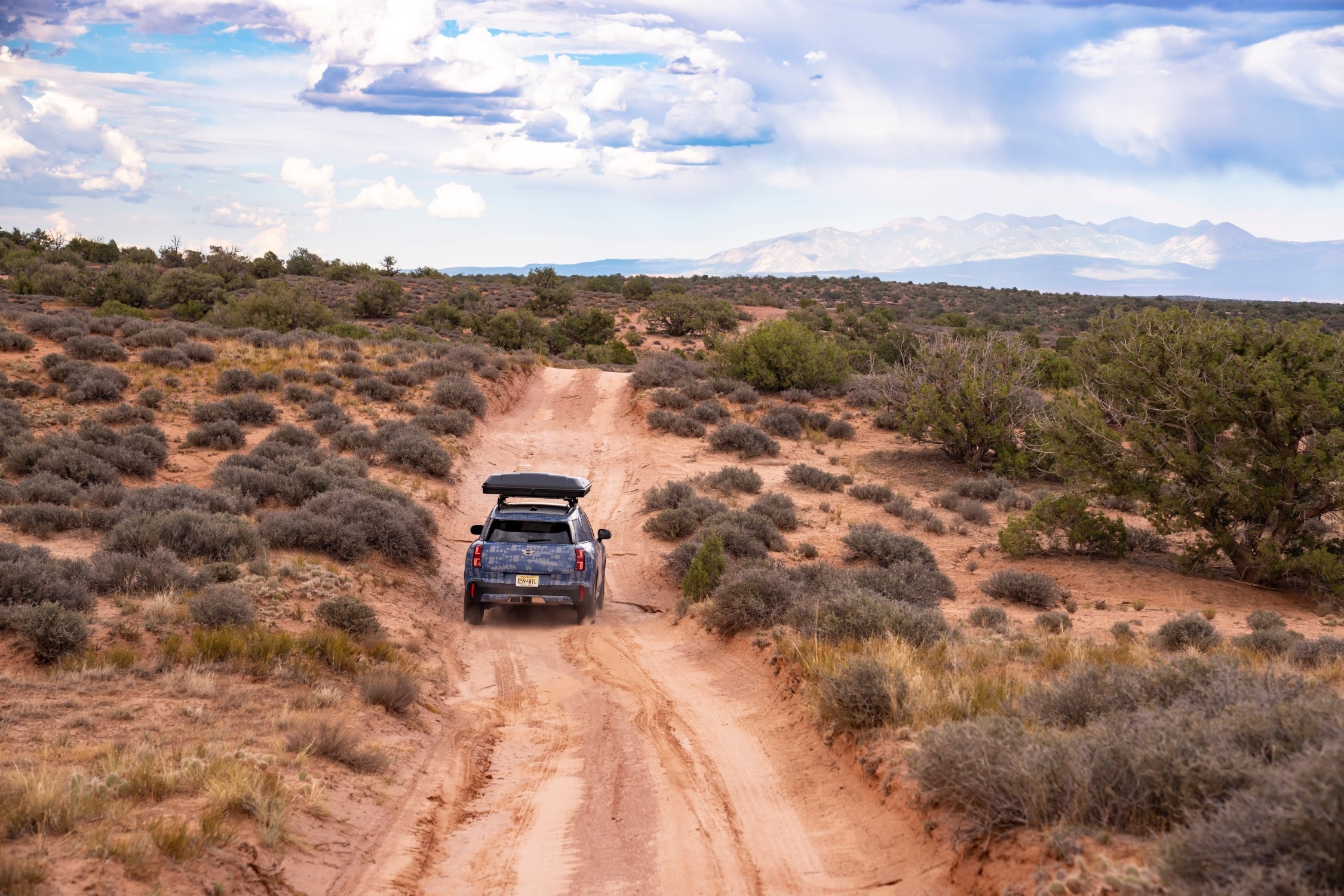 MINI Countryman visto pela traseira, a percorrer um trilho de terra batida numa  paisagem desértica, com vegetação rasteira e montanhas ao fundo 